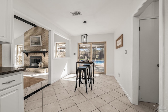 dining area featuring lofted ceiling, a brick fireplace, and light tile patterned floors