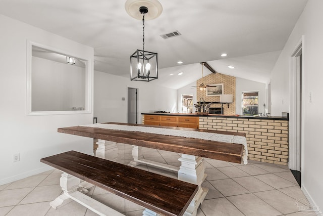 tiled dining area with a brick fireplace, vaulted ceiling, and ceiling fan