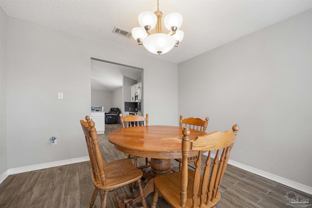 dining space featuring a textured ceiling, dark hardwood / wood-style flooring, and a notable chandelier