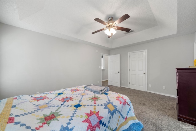 carpeted bedroom with a textured ceiling, ceiling fan, and a raised ceiling