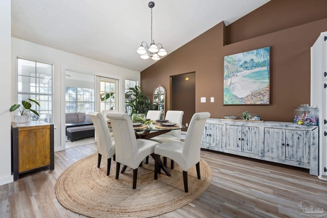 dining area with high vaulted ceiling, a chandelier, and light wood-type flooring