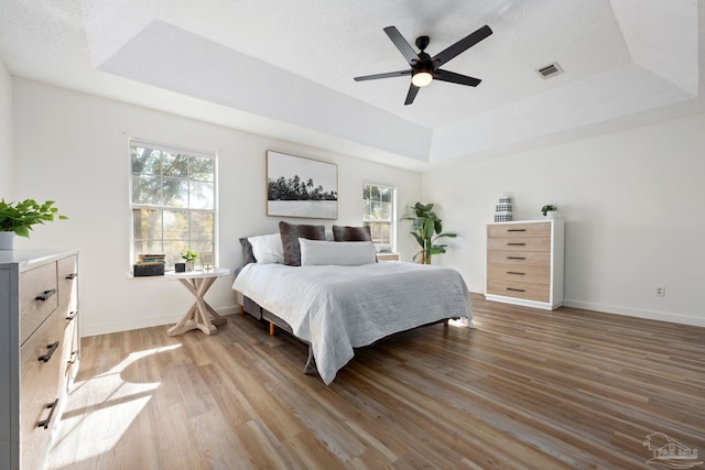 bedroom featuring ceiling fan, hardwood / wood-style flooring, and a tray ceiling