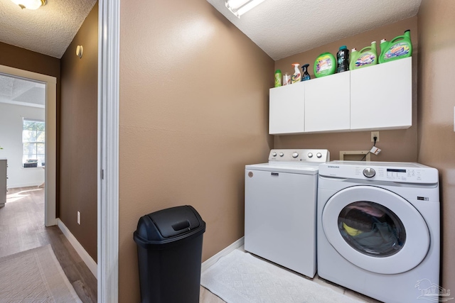 clothes washing area with light wood-type flooring, a textured ceiling, cabinets, and independent washer and dryer