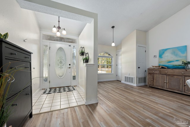 entryway featuring light wood-type flooring, a chandelier, and vaulted ceiling