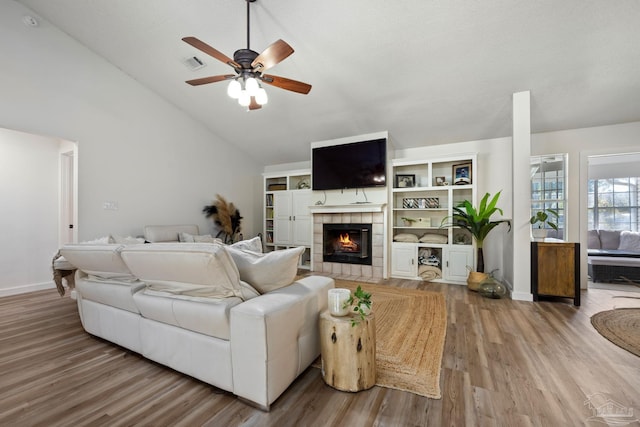 living room featuring ceiling fan, a tile fireplace, lofted ceiling, and wood-type flooring