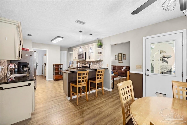 kitchen with tasteful backsplash, stainless steel appliances, white cabinetry, hanging light fixtures, and a breakfast bar area