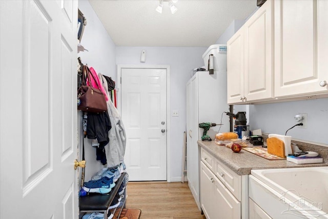 laundry room with sink, cabinets, light wood-type flooring, and a textured ceiling