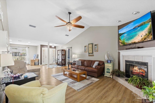 living room featuring a tiled fireplace, ceiling fan, light hardwood / wood-style flooring, and vaulted ceiling