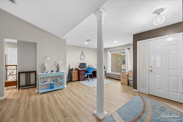 foyer entrance featuring a textured ceiling, light hardwood / wood-style floors, ornate columns, and vaulted ceiling