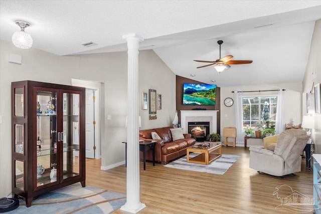 living room with ornate columns, ceiling fan, a textured ceiling, lofted ceiling, and a fireplace