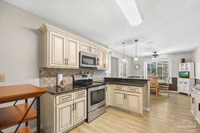 kitchen featuring hanging light fixtures, ceiling fan, appliances with stainless steel finishes, cream cabinetry, and kitchen peninsula