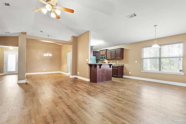 kitchen featuring visible vents, hanging light fixtures, light wood-style floors, a kitchen breakfast bar, and open floor plan