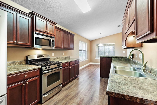 kitchen featuring appliances with stainless steel finishes, vaulted ceiling, a sink, a textured ceiling, and wood finished floors