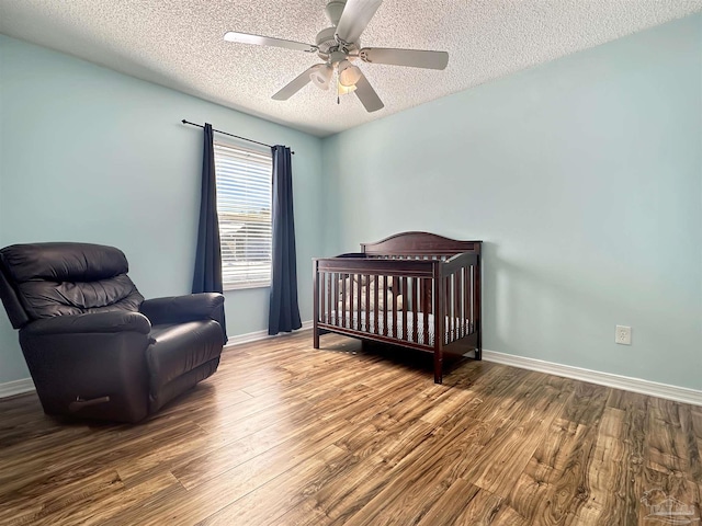 bedroom with ceiling fan, wood-type flooring, a textured ceiling, and a crib