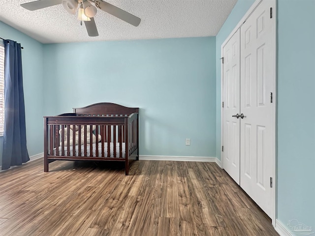 bedroom featuring ceiling fan, a nursery area, a textured ceiling, dark hardwood / wood-style flooring, and a closet