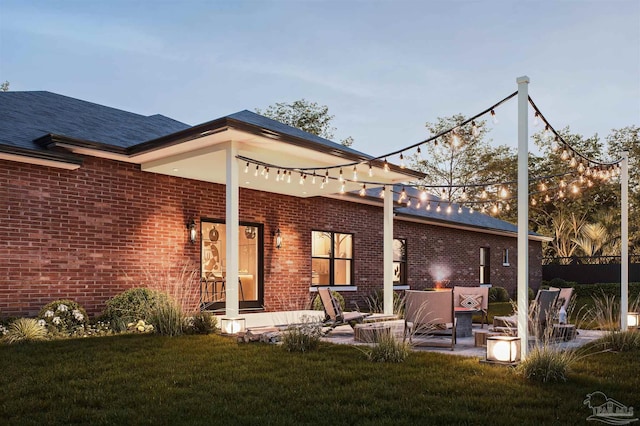 back house at dusk featuring a lawn and a patio area