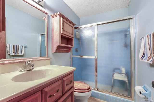 bathroom featuring a textured ceiling, toilet, a shower with door, and vanity