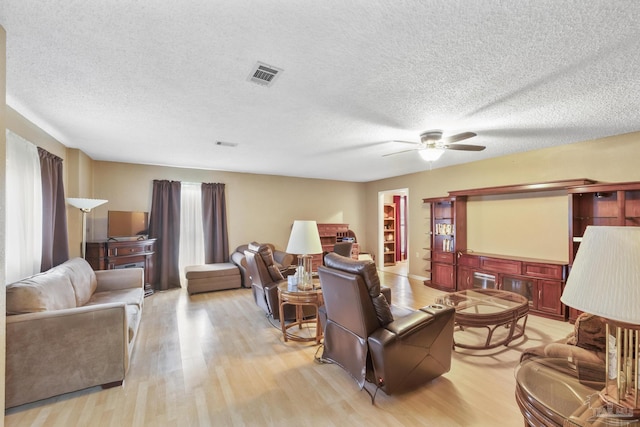 living room with ceiling fan, a textured ceiling, and light hardwood / wood-style flooring