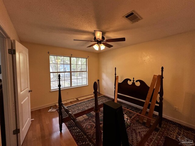 bedroom with ceiling fan, a textured ceiling, and dark hardwood / wood-style flooring