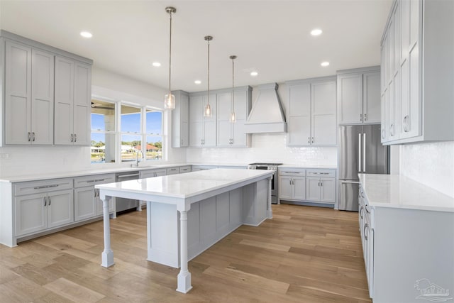 kitchen with premium range hood, gray cabinetry, light wood-type flooring, appliances with stainless steel finishes, and a kitchen island