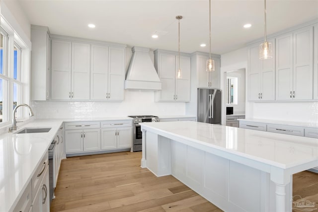 kitchen featuring a kitchen island, decorative light fixtures, sink, custom exhaust hood, and stainless steel appliances