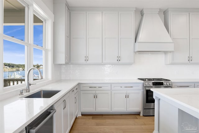 kitchen featuring sink, appliances with stainless steel finishes, white cabinetry, premium range hood, and light wood-type flooring