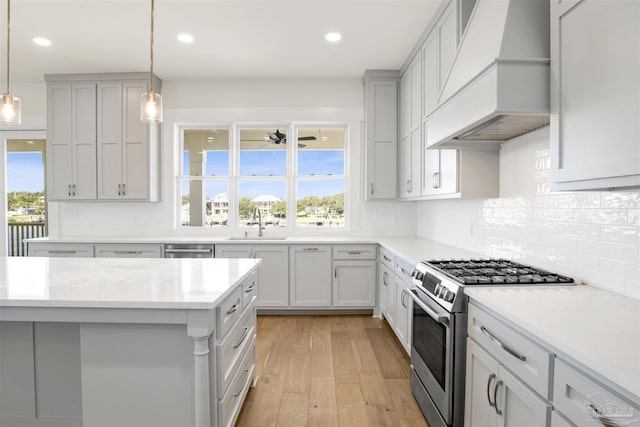 kitchen featuring sink, custom exhaust hood, light hardwood / wood-style flooring, appliances with stainless steel finishes, and pendant lighting