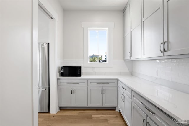 kitchen with gray cabinetry, light stone counters, stainless steel fridge, light hardwood / wood-style floors, and decorative backsplash