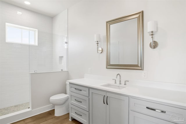 bathroom featuring hardwood / wood-style flooring, tiled shower, vanity, and toilet