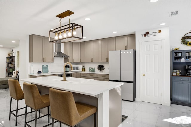 kitchen featuring decorative backsplash, freestanding refrigerator, marble finish floor, gray cabinets, and wall chimney range hood