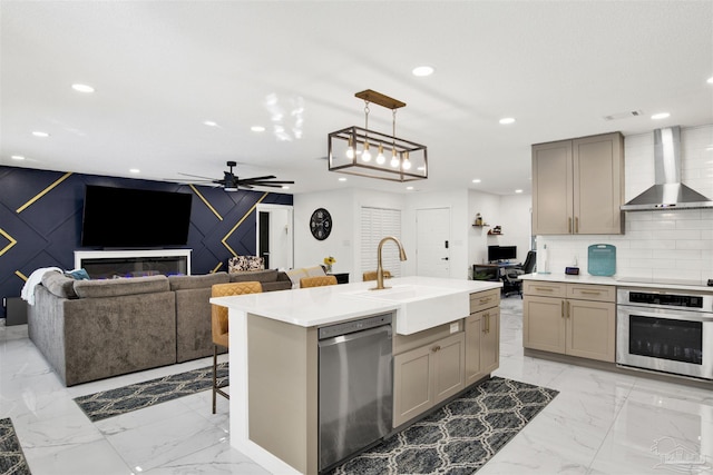 kitchen featuring marble finish floor, stainless steel appliances, gray cabinets, a sink, and wall chimney exhaust hood