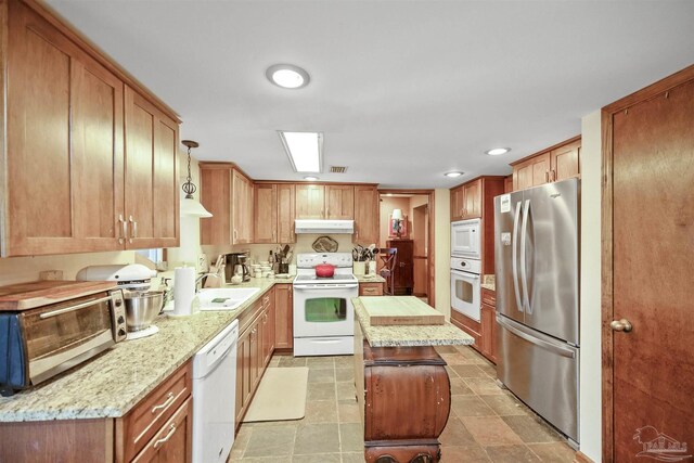 kitchen with pendant lighting, sink, a center island, light stone countertops, and white appliances