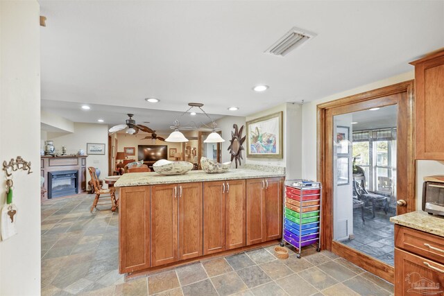 kitchen with ceiling fan, light stone countertops, kitchen peninsula, and hanging light fixtures