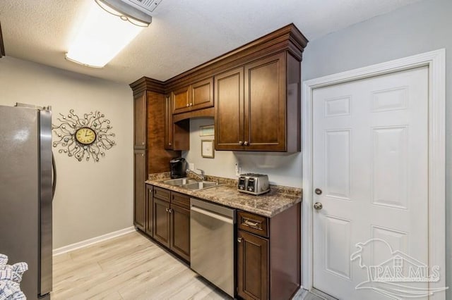 kitchen featuring sink, dark stone countertops, light wood-type flooring, stainless steel appliances, and a textured ceiling