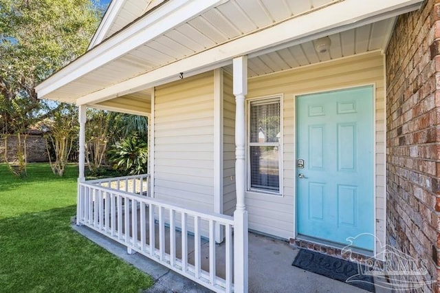 view of exterior entry featuring a porch and a lawn