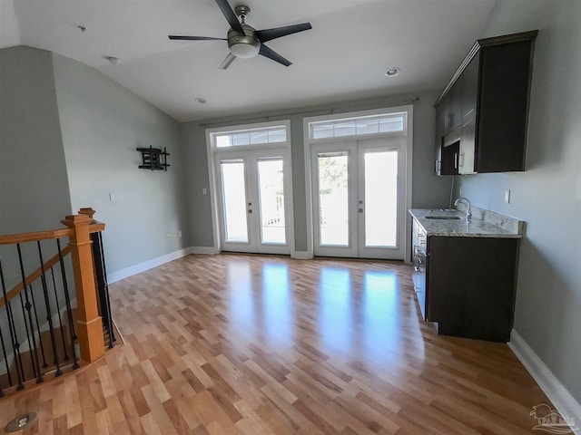 unfurnished living room with lofted ceiling, ceiling fan, sink, light hardwood / wood-style flooring, and french doors