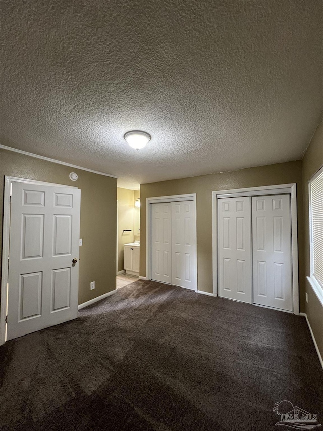 unfurnished bedroom with two closets, ensuite bathroom, a textured ceiling, and carpet