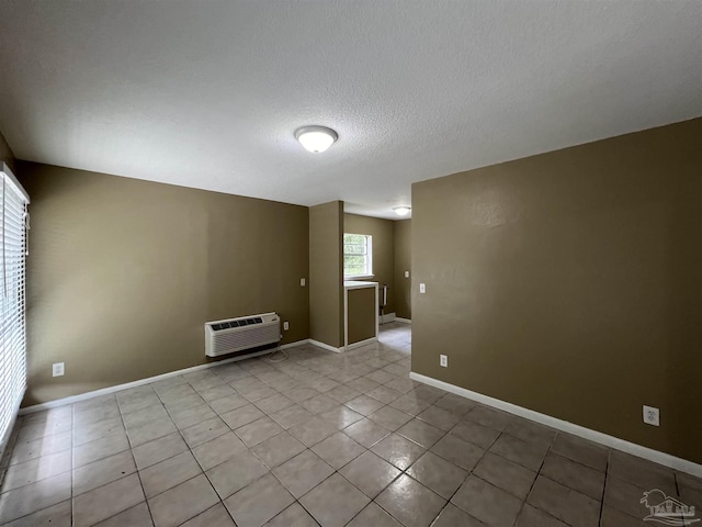 empty room featuring a wall mounted air conditioner, a textured ceiling, and light tile patterned flooring