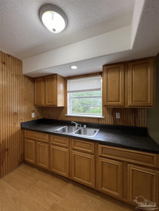 kitchen featuring sink, light wood-type flooring, a textured ceiling, and wood walls