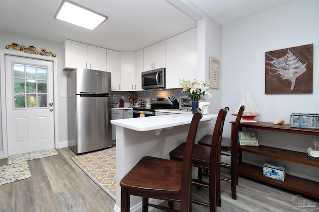 kitchen featuring light wood-type flooring, backsplash, kitchen peninsula, stainless steel appliances, and white cabinets