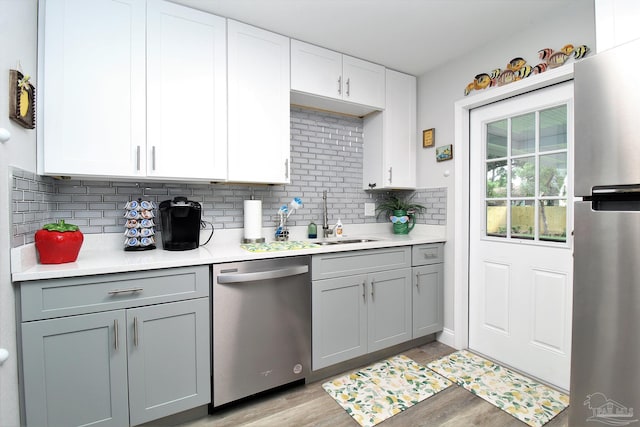 kitchen featuring appliances with stainless steel finishes, sink, light hardwood / wood-style floors, gray cabinets, and decorative backsplash