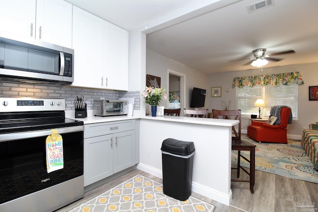 kitchen with kitchen peninsula, stainless steel appliances, backsplash, white cabinets, and light hardwood / wood-style floors