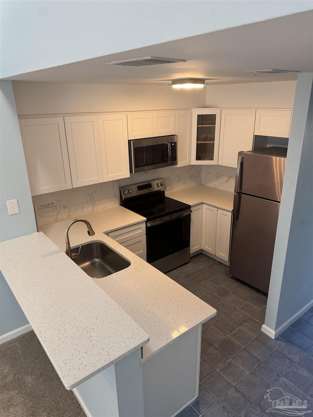 kitchen with a sink, appliances with stainless steel finishes, a peninsula, white cabinets, and glass insert cabinets