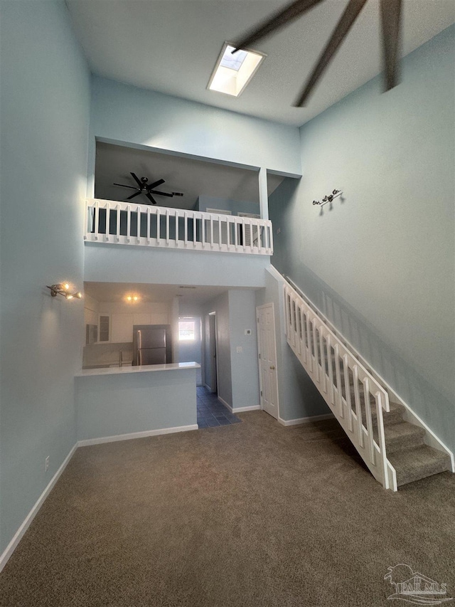 unfurnished living room with ceiling fan, baseboards, a towering ceiling, and carpet floors