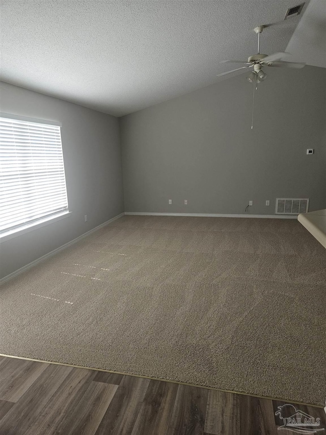 empty room featuring a textured ceiling, ceiling fan, dark wood-type flooring, and visible vents