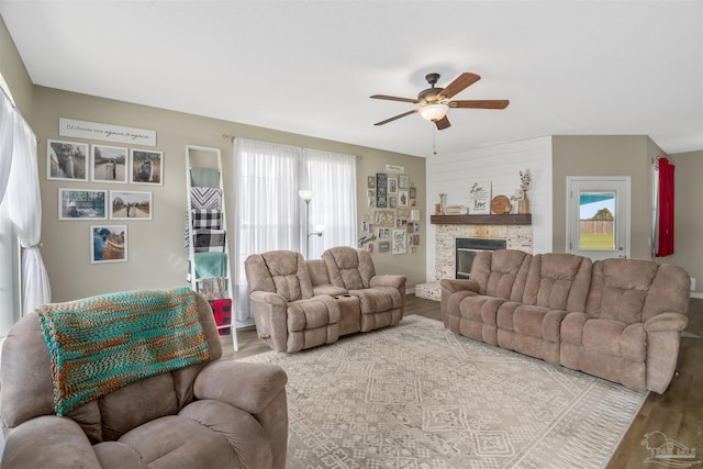 living room featuring ceiling fan, hardwood / wood-style flooring, and a stone fireplace