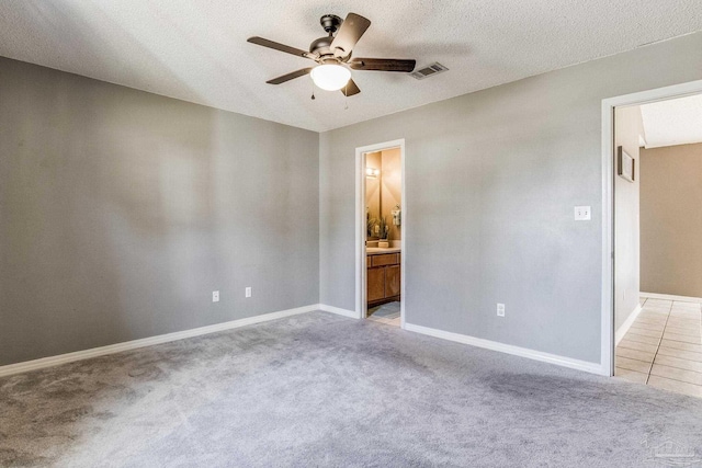 unfurnished bedroom with light carpet, ceiling fan, a textured ceiling, and ensuite bath