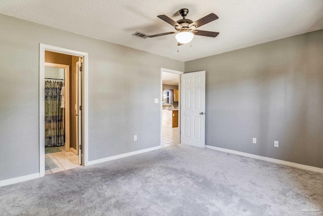 unfurnished bedroom featuring ceiling fan, light colored carpet, connected bathroom, and a textured ceiling