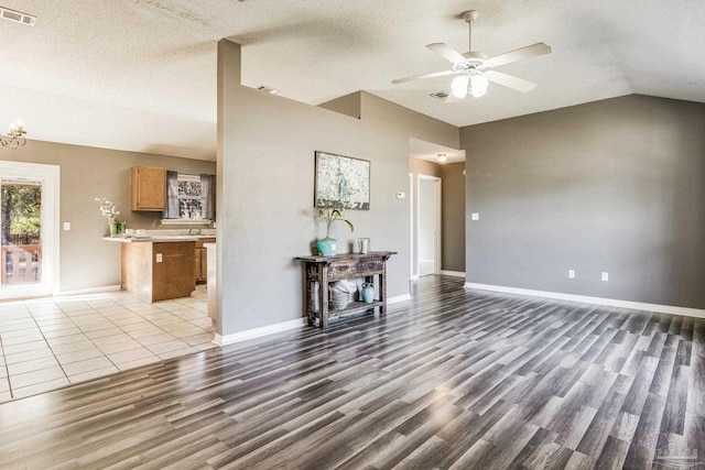 interior space featuring lofted ceiling, ceiling fan with notable chandelier, a textured ceiling, and light hardwood / wood-style floors