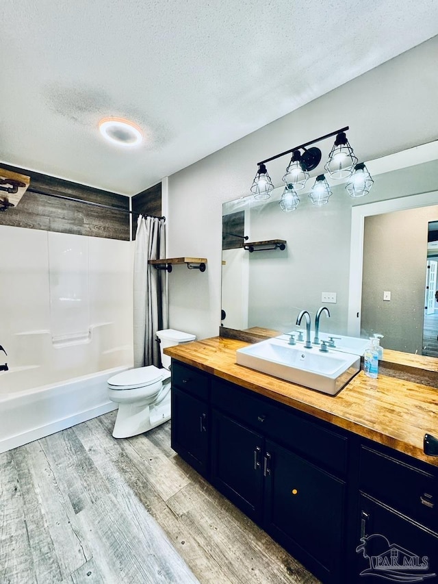 full bathroom with a textured ceiling, shower / tub combo with curtain, hardwood / wood-style floors, toilet, and vanity